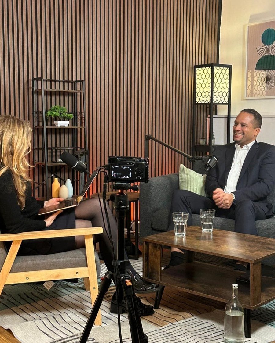 Louis Stedman-Bryce laughing during a recorded interview in a wood-panelled studio.